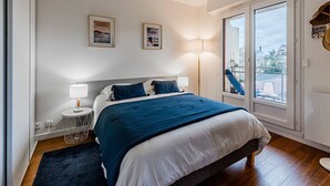 Une chambre à coucher avec un lit, des lampes de chevet, une fenêtre donnant sur un beau paysage et deux tableaux encadrés accrochés au mur.