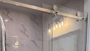 En dusch med glasväggar, väggar klädda i marmor och ett golv med hexagonformade kakelplattor.