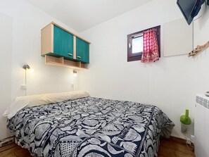 A bedroom with a bed, a small window with red curtains, a green cabinet above the bed, and a wall-mounted TV. - Cozy retreat in Valloire - 4 pers, pets welcome (Valloire)