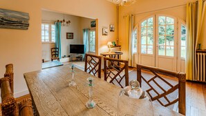 A dining area with a wooden table, chairs, a chandelier, and a view through a large window. - ARCACHON, LES ABATILLES : A 450 M DE LA CELEBRE SOURCE DES ABATILLES ! (Arcachon)