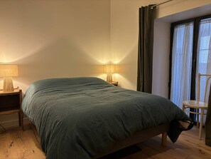 Ein Schlafzimmer mit einem Bett, zwei Nachttischlampen, einem Sessel und einem Fenster mit Vorhängen.