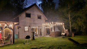 A rustic wooden house with a covered porch and string lights, surrounded by a well-maintained lawn. - Large Holiday Home, Salt Cave, Sauna, Jacuzzi (Lipusz)
