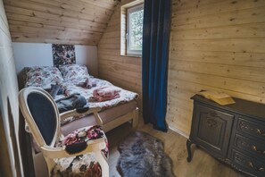 Una camera da letto con soffitto in legno, un letto con biancheria a fiori, una cassettiera e una finestra con tende.