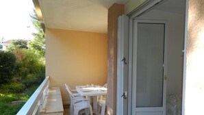 Ein Balkon mit Tisch und Stühlen, eine Schiebetür aus Glas und Blick auf Grünflächen.