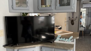 Cozinha com armários cinza, uma televisão preta e bancada com uma placa que diz 'Beach'.