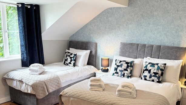 A modern hotel room with two beds, a large window with curtains, a grey textured wall, and a wooden floor. - No 27 Killarney Holiday Village - Great Location (Killarney)