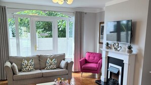 A living room with a sofa, a pink armchair, a fireplace, and a TV mounted on the wall. - No 27 Killarney Holiday Village - Great Location (Killarney)