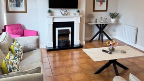 A living room with a fireplace, a flat-screen TV, a pink sofa, and a coffee table. - No 27 Killarney Holiday Village - Great Location (Killarney)