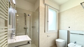 Moderni kylpyhuone, jossa on lasiseinällä varustettu suihku, valkoinen pesuallas, wc ja bidee.