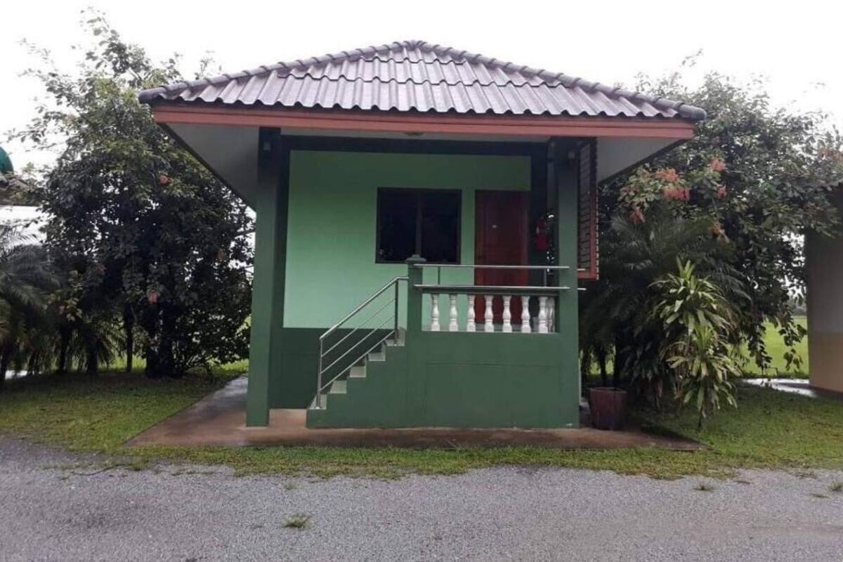 A small, single-story building with a green exterior and a tiled roof. It features a small porch with a railing and a single door.
