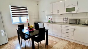 A modern kitchen with white cabinets, a dining table with chairs, a fruit bowl, and a microwave. - Adorable 1-bedroom apartment in charming Dugi Rat (Dugi Rat)
