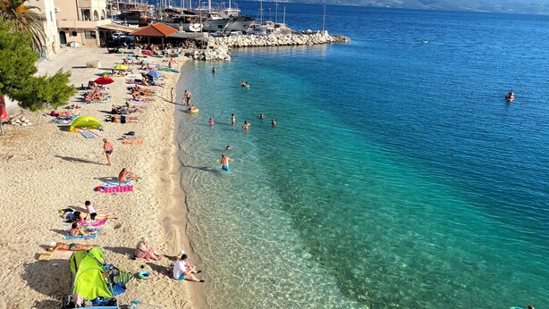 A beach with clear water, people sunbathing, and boats docked nearby. - Adorable 1-bedroom apartment in charming Dugi Rat (Dugi Rat)