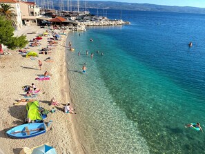A beach with clear water, people sunbathing, and boats docked nearby. - Adorable 1-bedroom apartment in charming Dugi Rat (Dugi Rat)