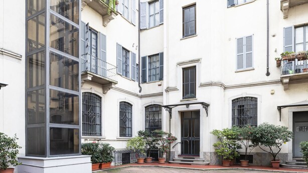 Un cortile con un edificio bianco, grandi finestre, una porta nera e piante in vaso.