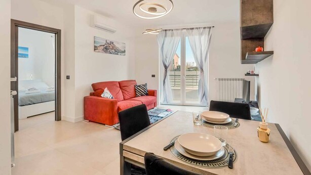 Un salon moderne avec un canapé rouge, une table à manger dressée avec des assiettes et des couverts, et une grande fenêtre avec des rideaux.