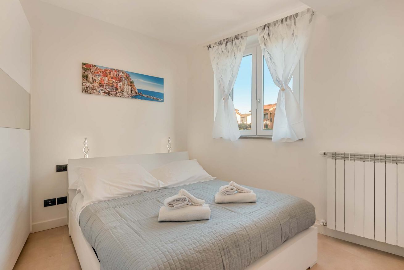 A bedroom with a bed, a painting, a window with curtains, and a radiator.