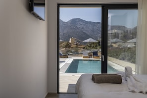 A bedroom with a large sliding glass door leading to a pool area with a mountain view. - Superior Villa Celeste - Sea View and Private Pool (CQ9M+26M Geropotamos, Greece)