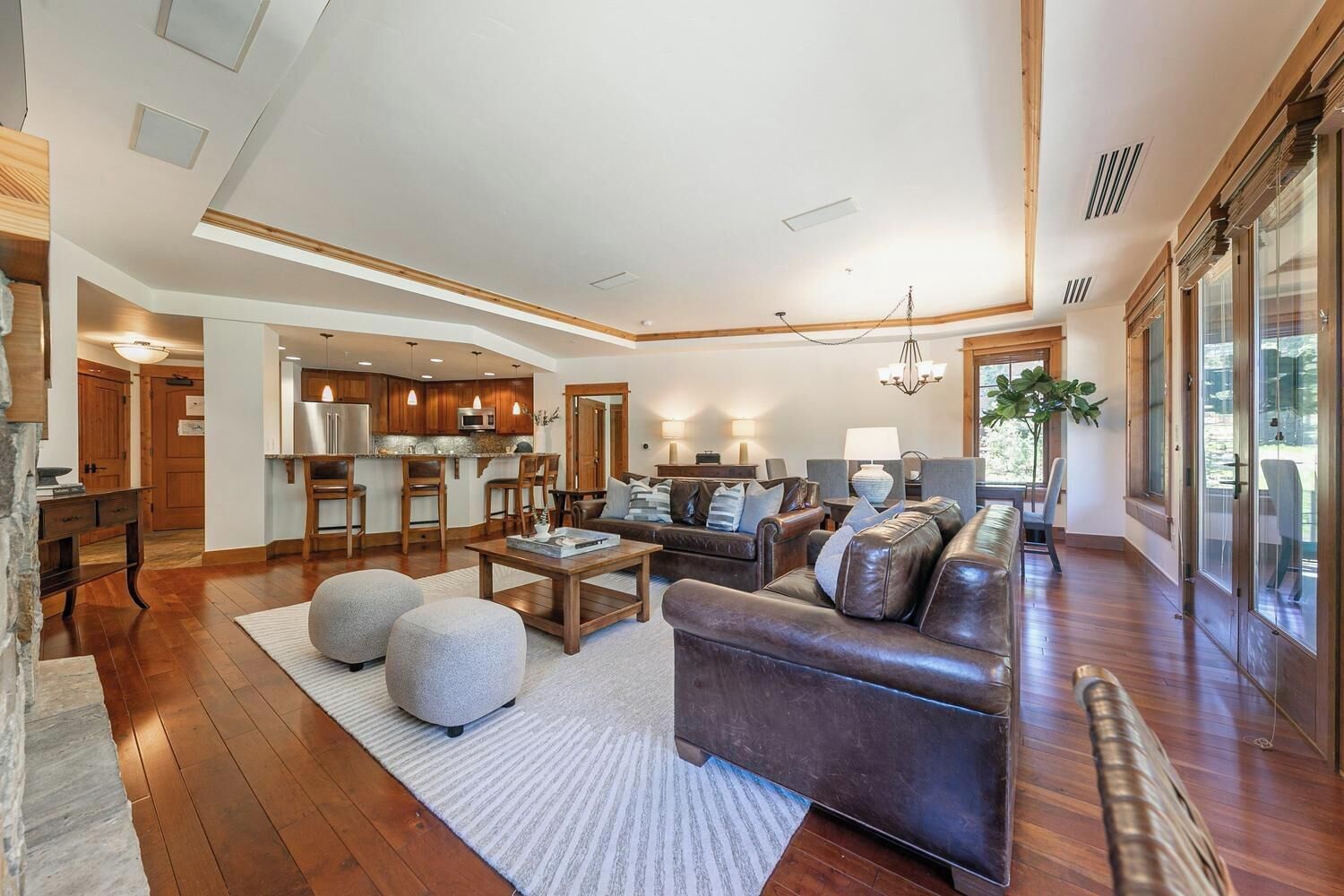 A spacious living room with a fireplace, a kitchen in the background, and large windows.