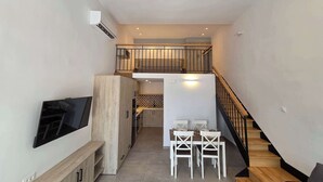 Un apartamento moderno con comedor, cocina y una escalera que sube a un altillo.