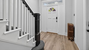Un couloir doté d’un plancher en bois, de murs blancs, d’un radiateur noir et d’une porte blanche avec un vitrage.