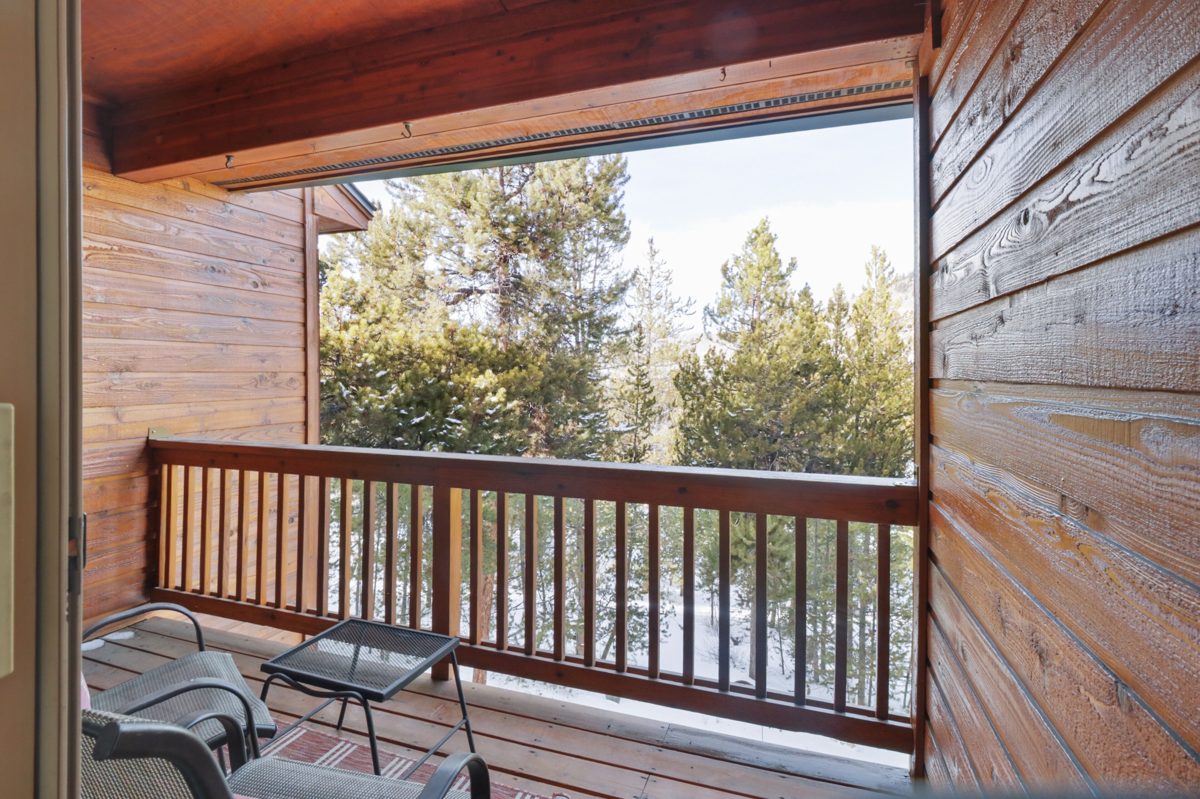 A wooden deck with a railing, two metal chairs, and a table.