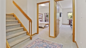 A hallway with a carpeted staircase, a bed in the adjacent room, and a door leading to another room. - 97 Lookout Ridge 2 Bedroom Townhouse (Dillon)