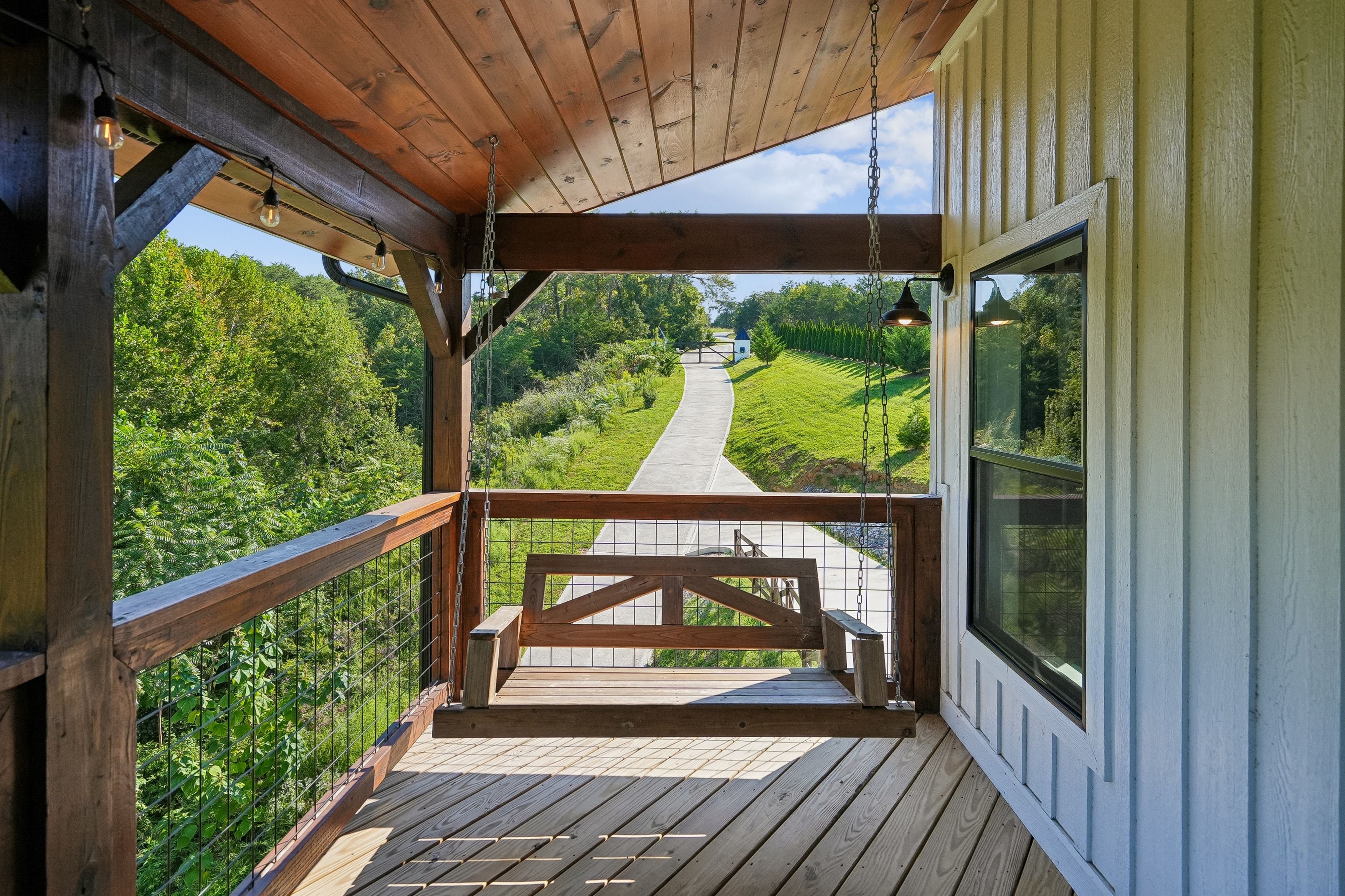 A wooden deck with a metal railing overlooking a paved path and greenery.