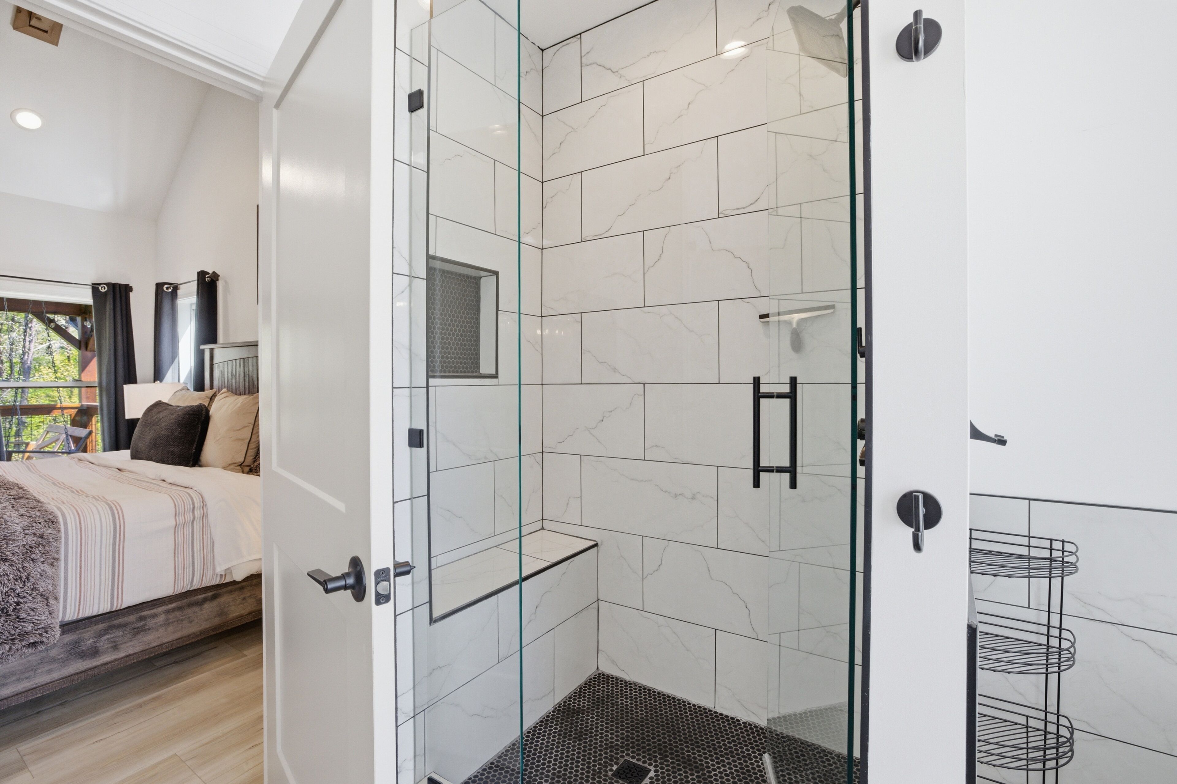 A modern bathroom with a glass shower enclosure, white marble tiles, and a visible showerhead.