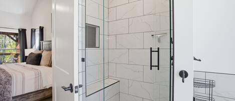 A modern bathroom with a glass shower enclosure, white marble tiles, and a visible showerhead.