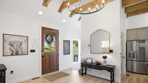 Ein modernes Interieur mit Holzboden, einem schwarzen Konsolentisch, einem großen Spiegel und einem Edelstahl-Kühlschrank.