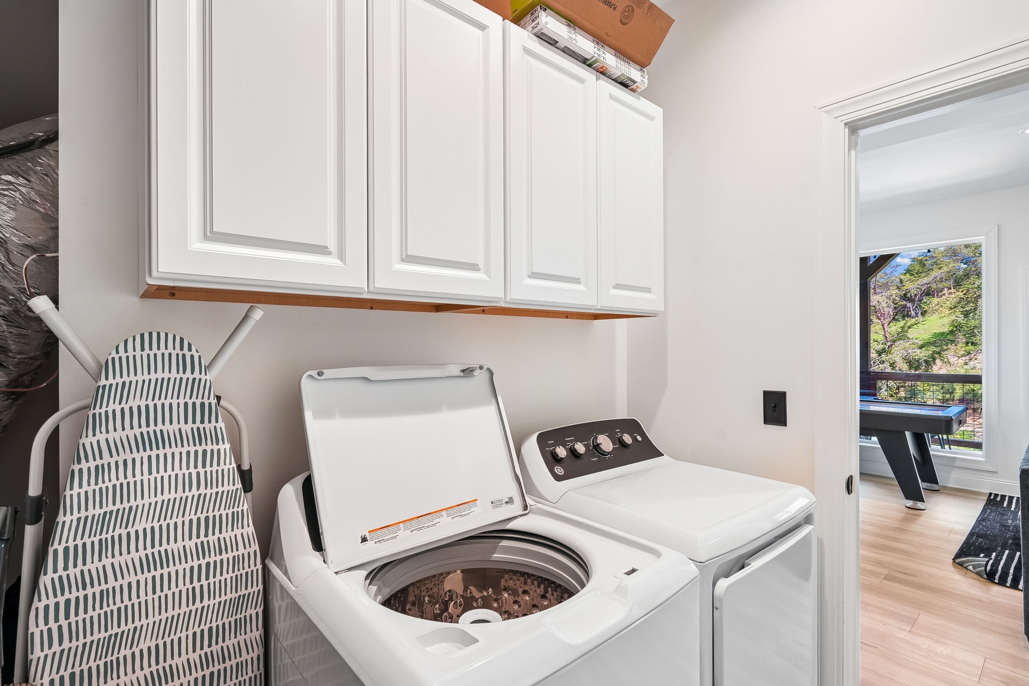 A laundry room with a washing machine, an ironing board, and a cabinet above.