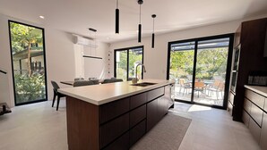 Een moderne keuken met een groot eiland, inbouwapparatuur en grote ramen met uitzicht op de omgeving.
