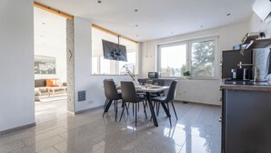 Moderni keittiö, jossa on ruokailutila, suuret ikkunat ja litteänäyttöinen televisio.