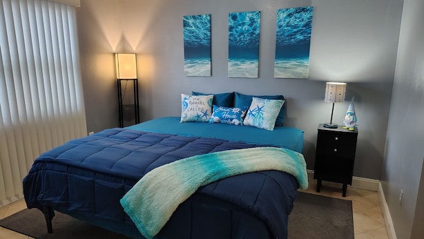 Un dormitorio con cama, mesita de noche, lámpara y decoración en la pared.