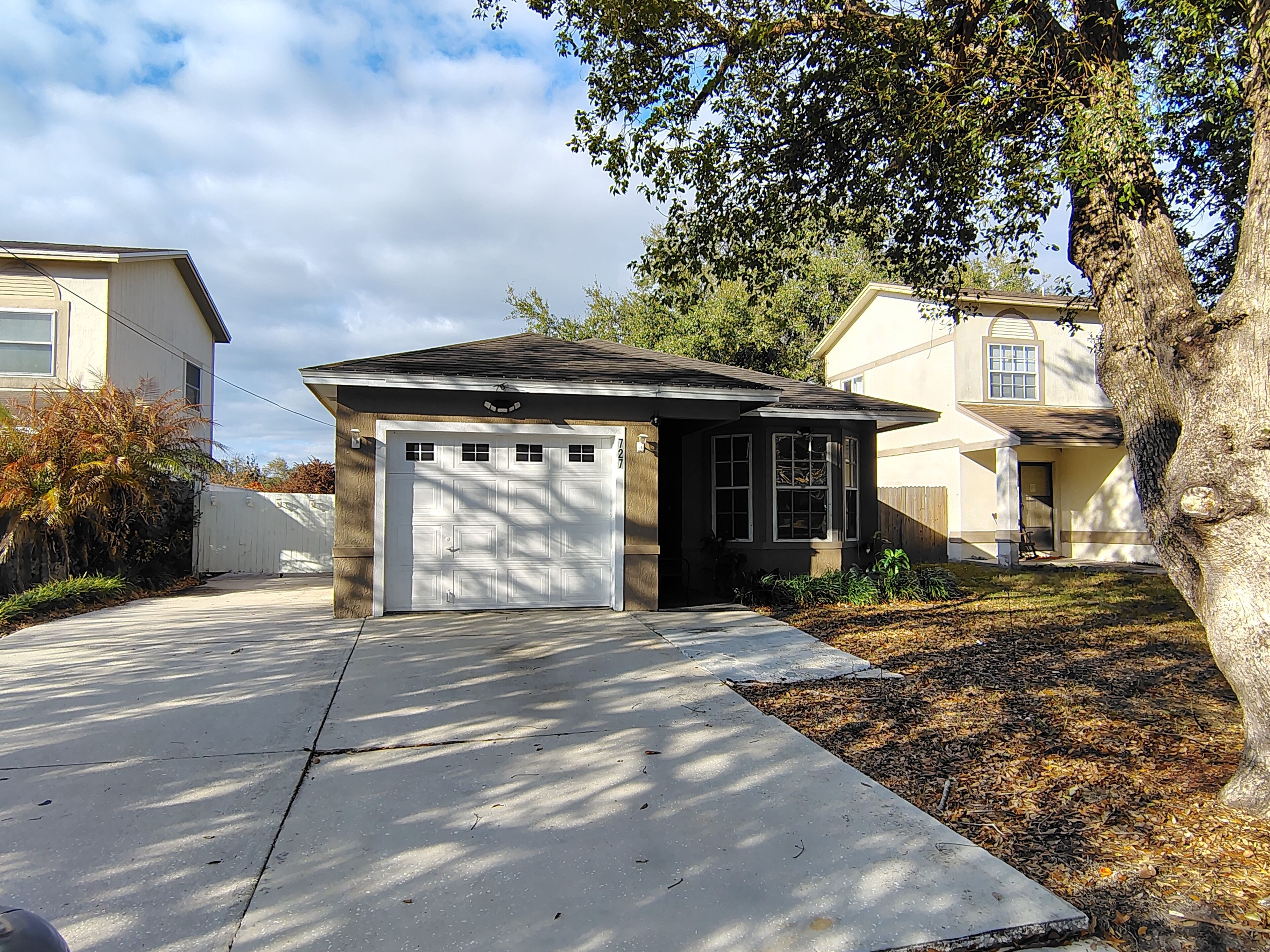 A residential garage with a small attached shed, a driveway, and a mature tree.
