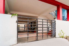 Une entrée fermée par un portail en métal, un escalier et un pot de fleurs.