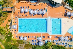 Eine Vogelperspektive auf ein Resort mit zwei Schwimmbecken, Liegestühlen und Sonnenschirmen.