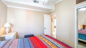 Un dormitorio con cama, mesita de noche, lámpara y una puerta que da a otra habitación.