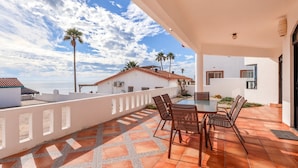 Una terraza con una mesa y sillas, un edificio blanco y vistas al mar.