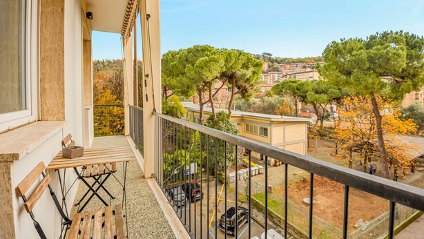 Ein Balkon mit Tisch und Stühlen, mit Blick auf einen Parkplatz und Gebäude mit Bäumen.