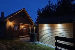 Eine Holzlaube mit Veranda und Lichterkette, eine kleine Werkstatt und eine Bank im Vordergrund.