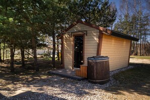 Une petite cabane en bois avec une porte et une poubelle devant.