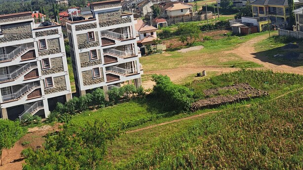 A residential area with multi-story buildings, a dirt path, and green fields.