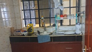 Una cocina con una silla de plástico azul, una cesta de tomates y un cilindro de gas.