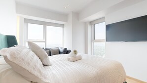 A modern bedroom with a large bed, two windows, a flat-screen TV, and a view of the city. - Start 2026 in a penthouse with amenities (Ciudad de México)