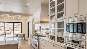 A modern kitchen with white cabinetry, stainless steel appliances, and a large island with a sink. - Sleeps 58! Parade Home! 30 Person Spa! (St. George)