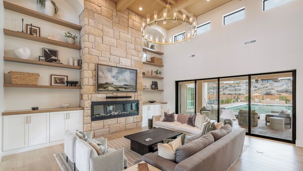 A modern living room with a stone fireplace, a large flat-screen TV, and a view of a pool. - Sleeps 58! Parade Home! 30 Person Spa! (St. George)