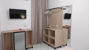 A hotel room with a flat-screen TV, a mini-fridge, a wooden wardrobe, a mirror, and a curtain. - Vila REJANA (Ksamil)
