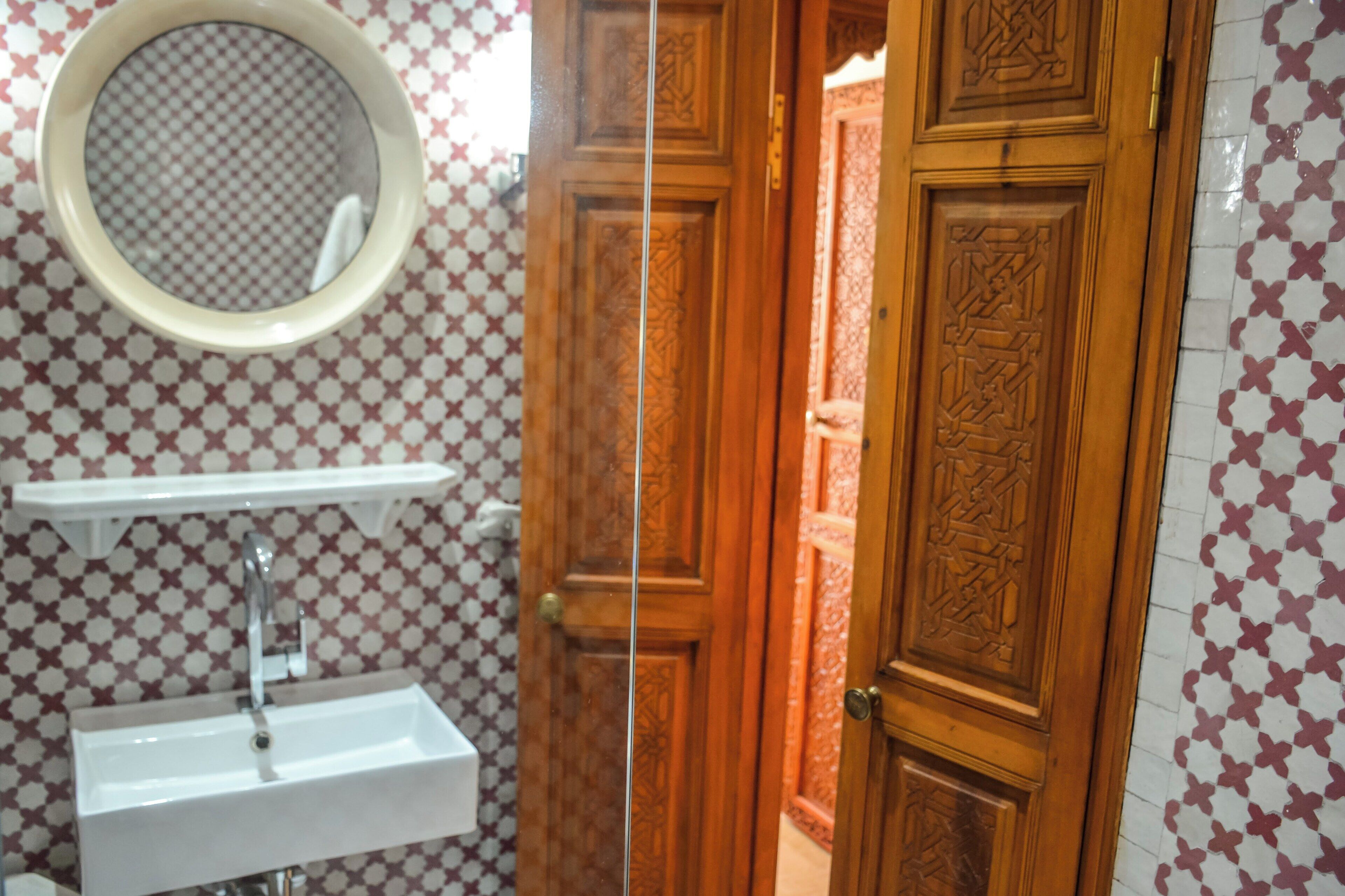 A bathroom with a sink, mirror, and patterned walls.