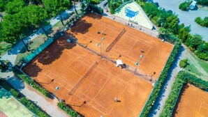 Luftaufnahme eines Tennisplatzes, umgeben von Grünflächen und einem Parkplatz.